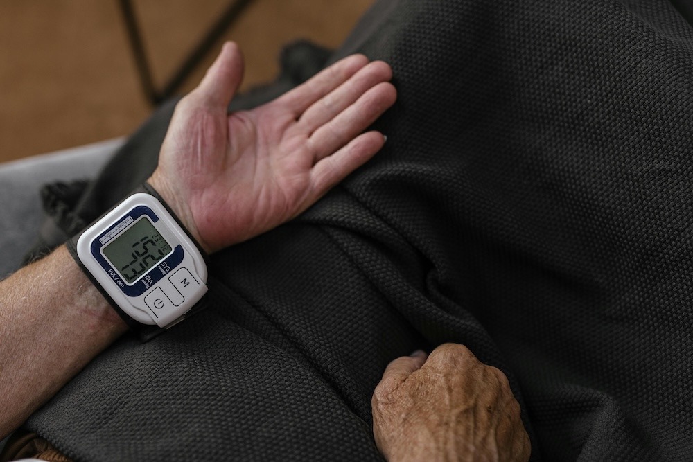 Eine Person misst den Blutdruck mit einem Handgelenk-Blutdruckmessgerät auf einer Couch.
