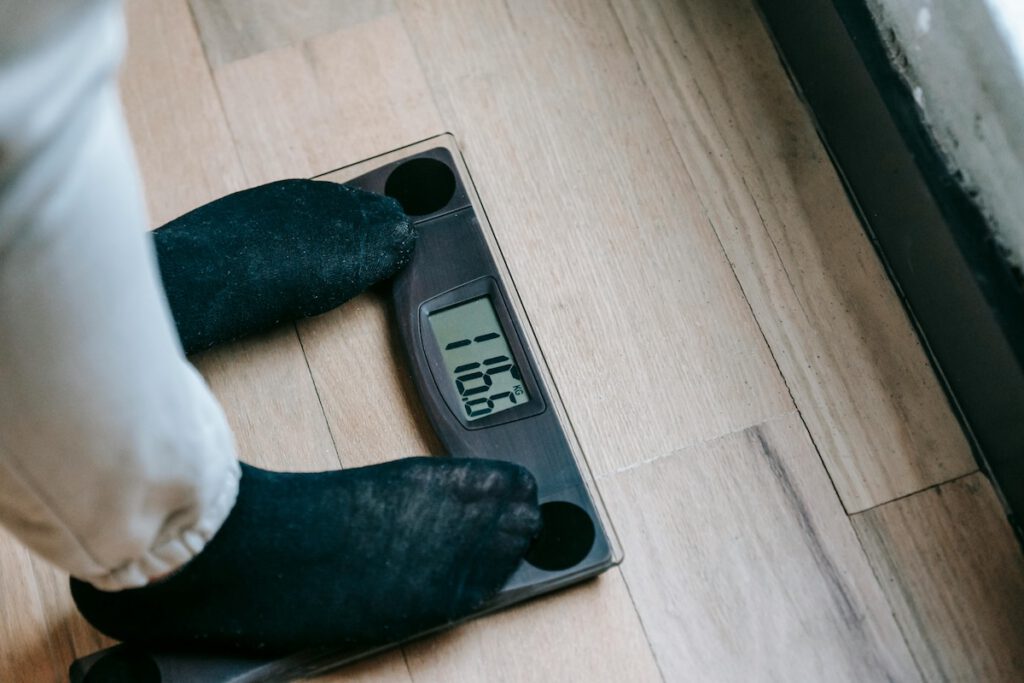 Person auf einer Körperfettwaage, die ein Gewicht von 110,5 kg anzeigt.