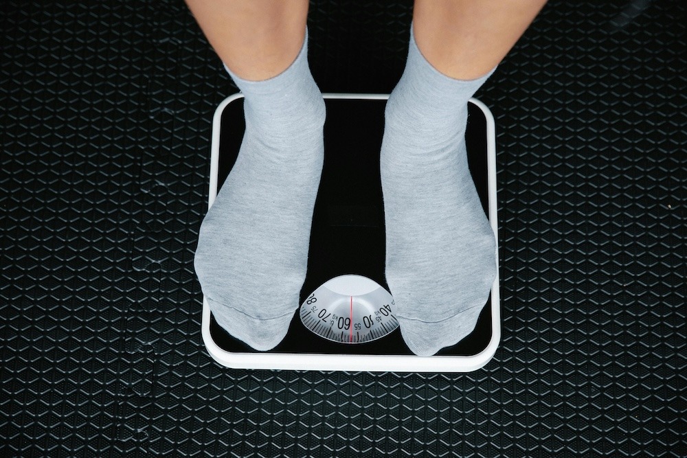 Person auf einer mechanischen Personenwaage mit grauen Socken, zeigt Gewicht auf analoger Skala an.